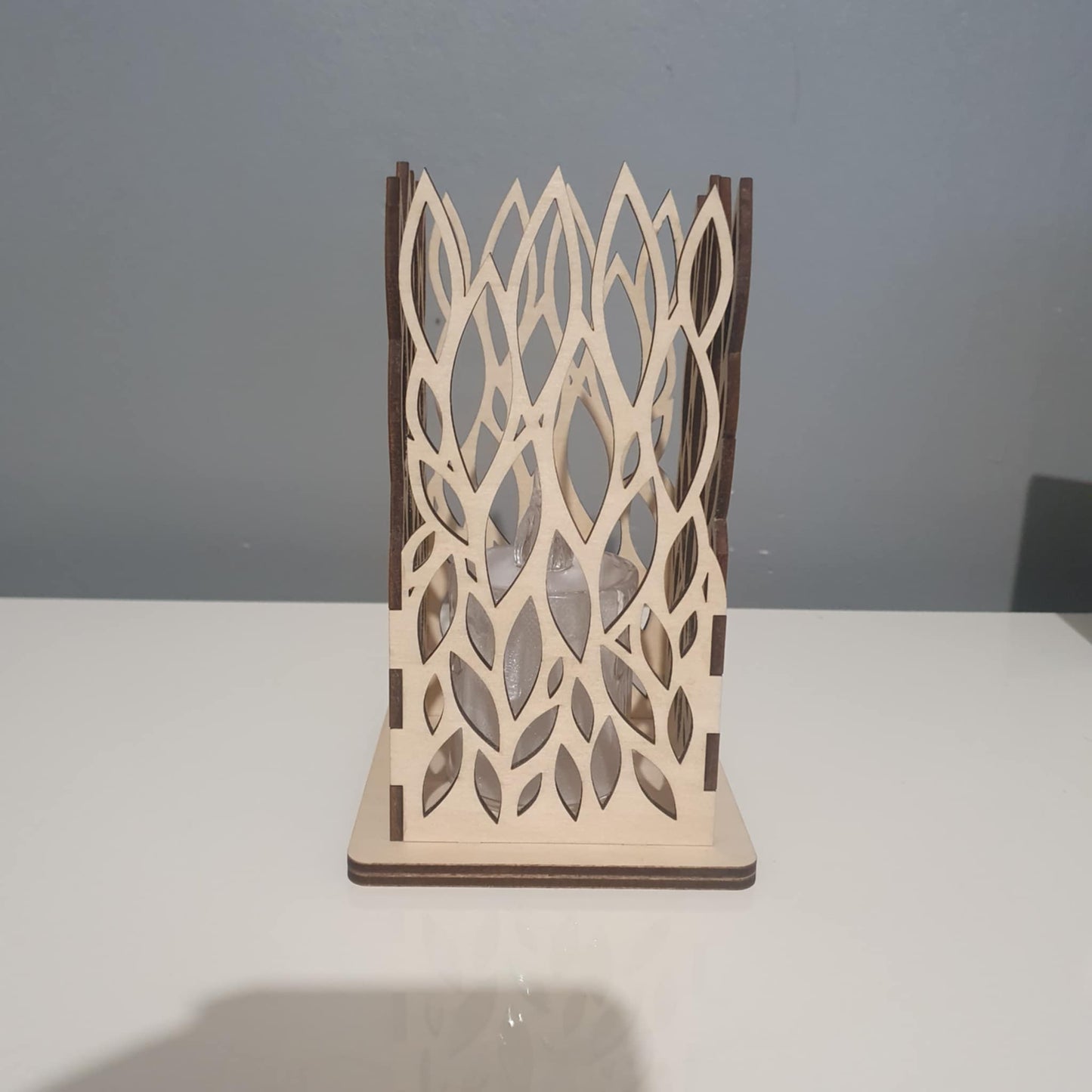 Photophore carré en bois avec motif de feuilles découpé au laser, éclairé par une bougie LED dans l'obscurité.