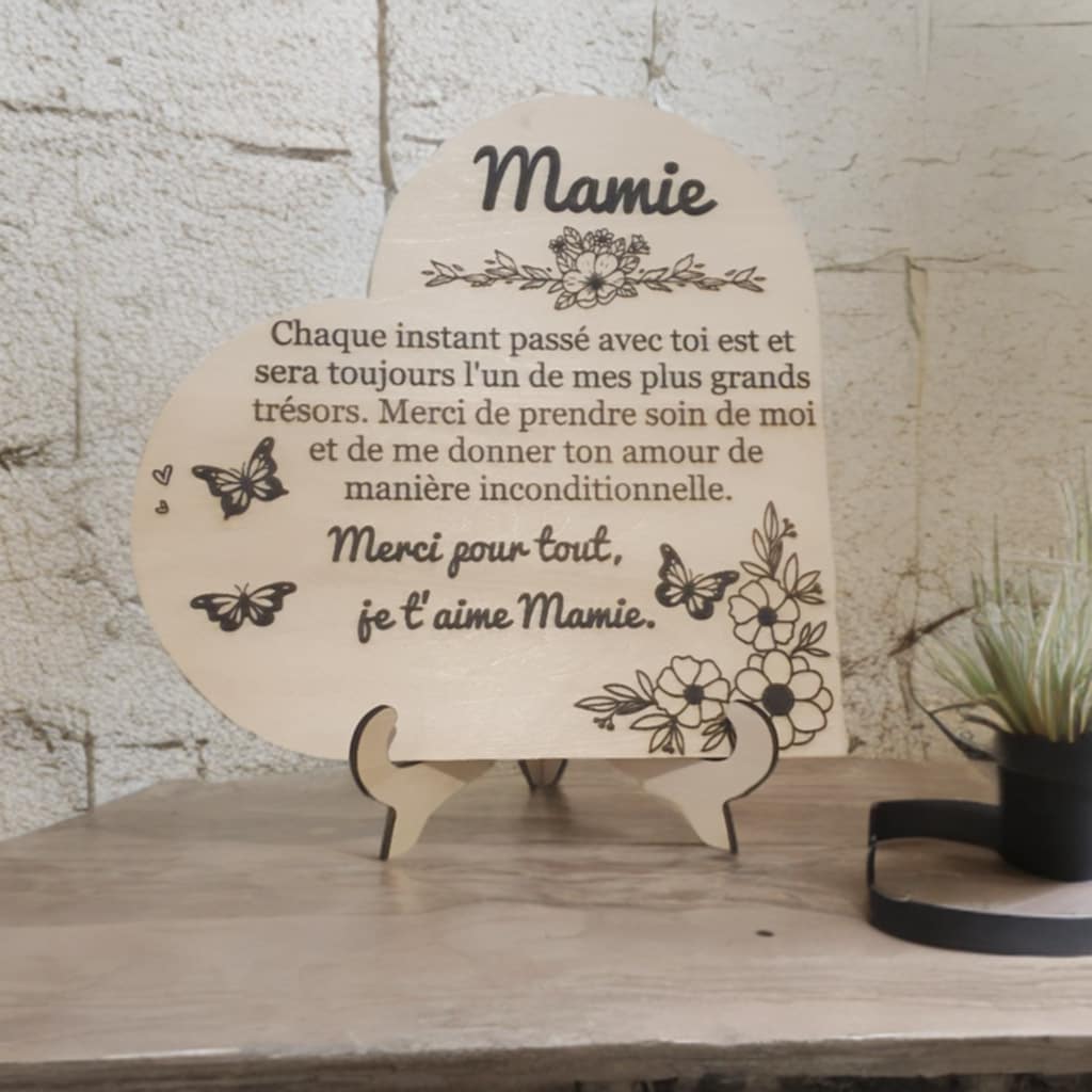 Plaque décorative en bois en forme de cœur avec gravure personnalisée pour Mamie, décorée de fleurs et papillons, posée sur son support.