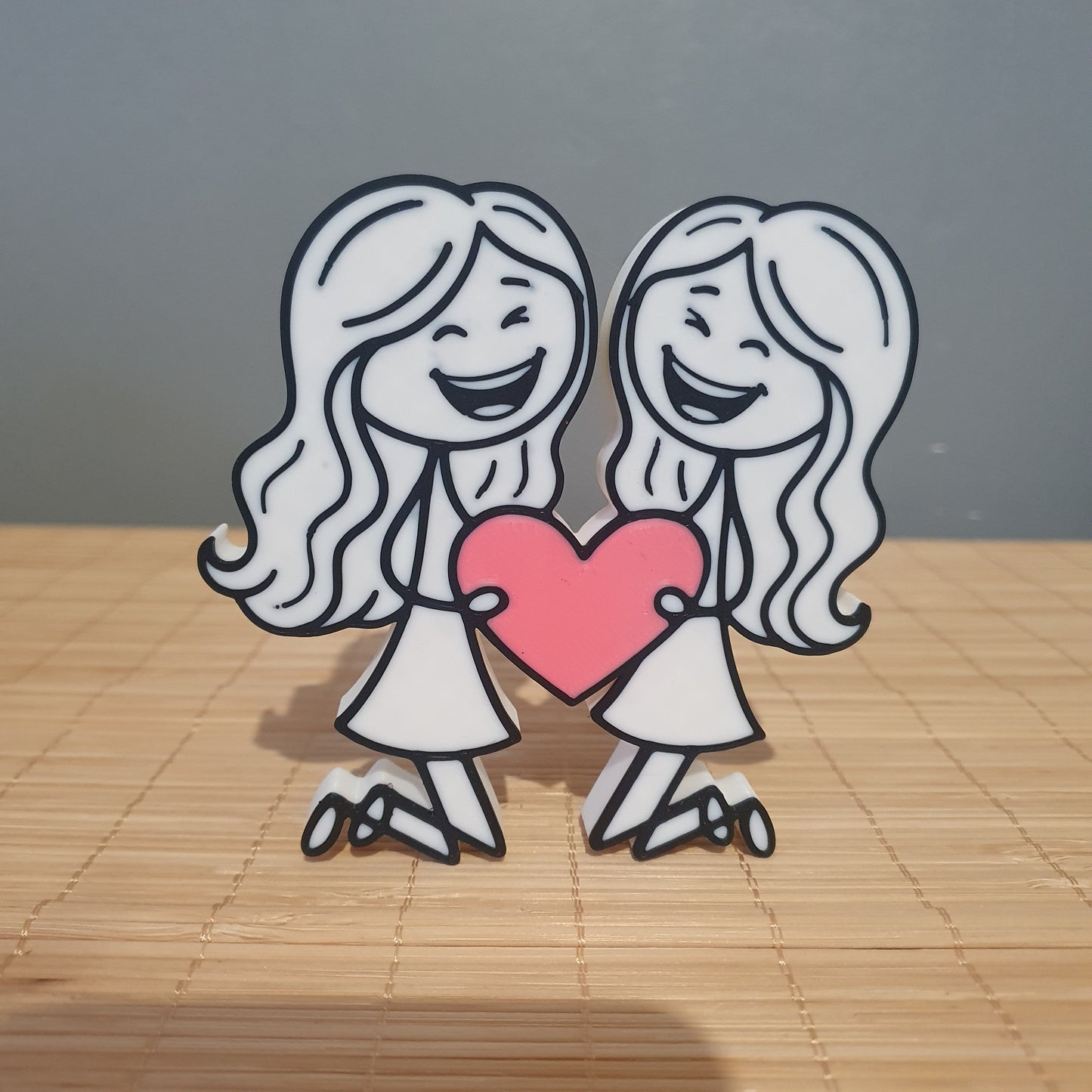 Décoration 3D inclusive représentant deux femmes avec de longs cheveux tenant un cœur rose.