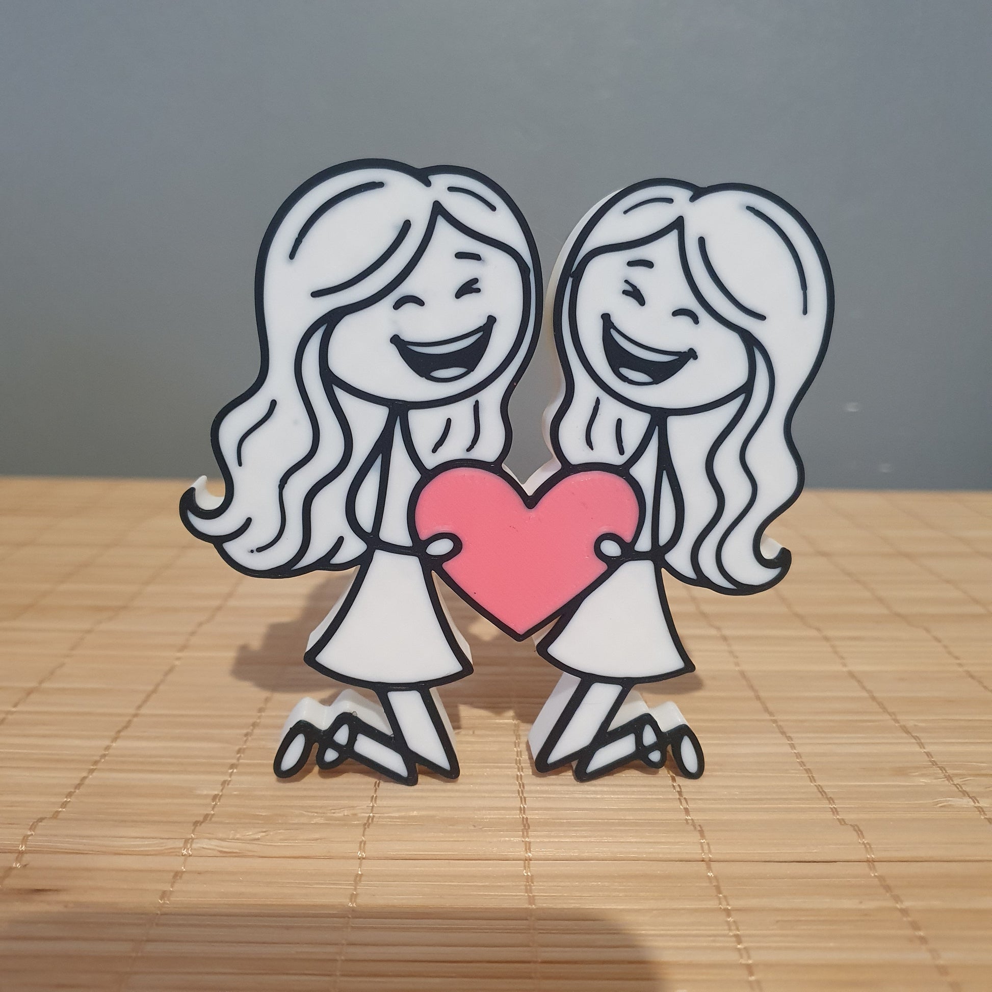 Décoration 3D inclusive représentant deux femmes avec de longs cheveux tenant un cœur rose.