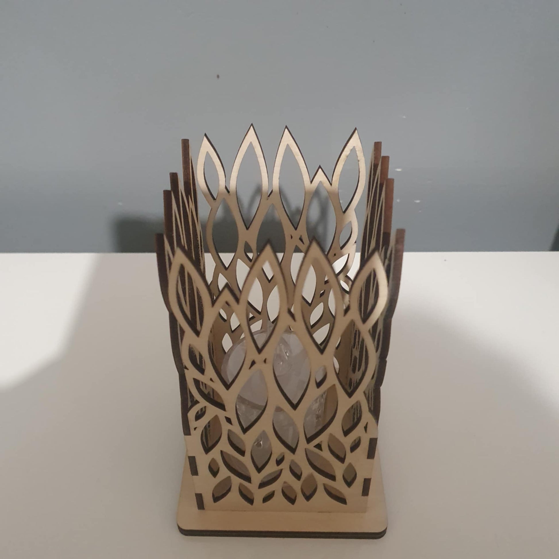 Photophore carré en bois avec motif de feuilles découpé au laser, éclairé par une bougie LED dans l'obscurité.