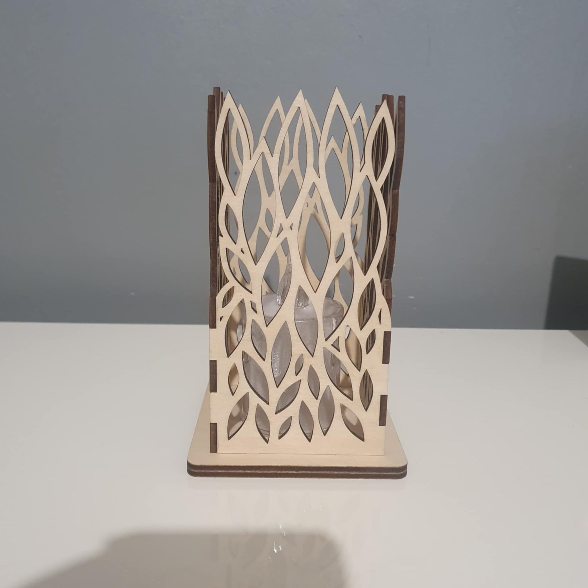 Photophore carré en bois avec motif de feuilles découpé au laser, éclairé par une bougie LED dans l'obscurité.