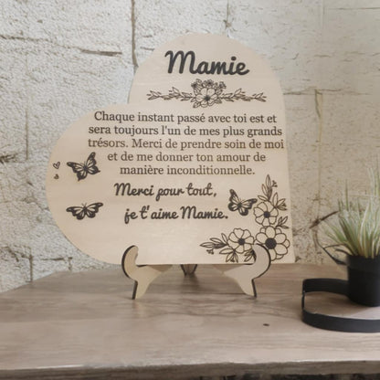 Plaque décorative en bois en forme de cœur avec gravure personnalisée pour Mamie, décorée de fleurs et papillons, posée sur son support.